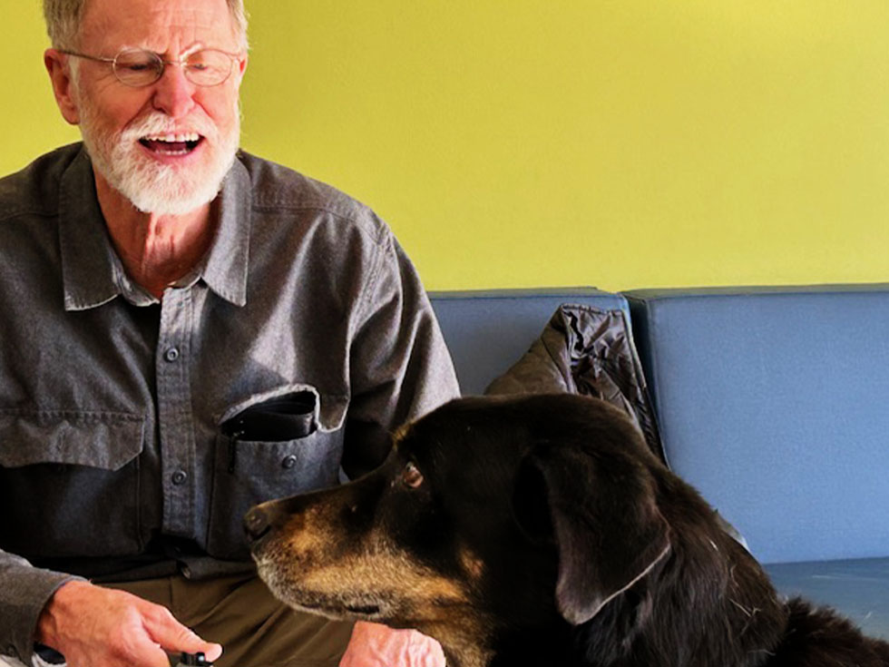 dog in profile with older man smiling in the background sitting in an armchair